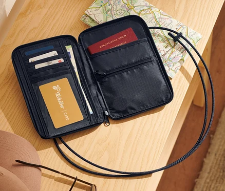 Pochette tour de cou noire ouverte avec cartes, passeport et carte sur une table en bois.