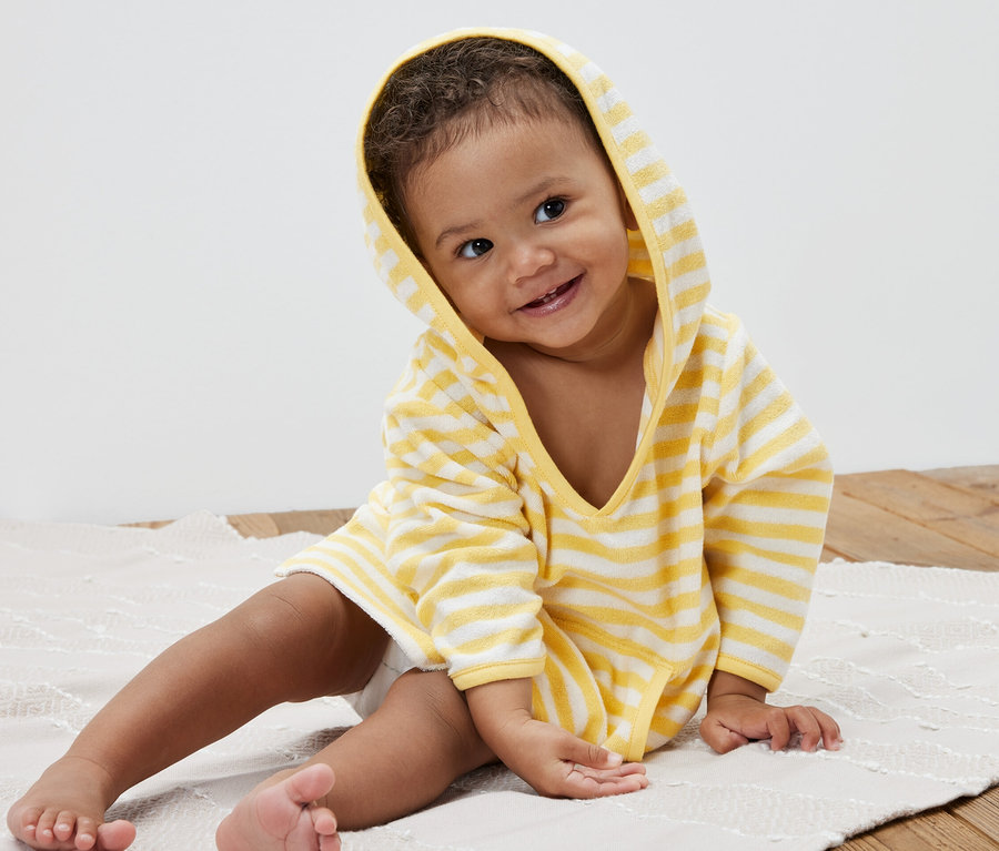 Un enfant souriant est assis sur un tapis et porte un poncho rayé en tissu éponge pour enfant.