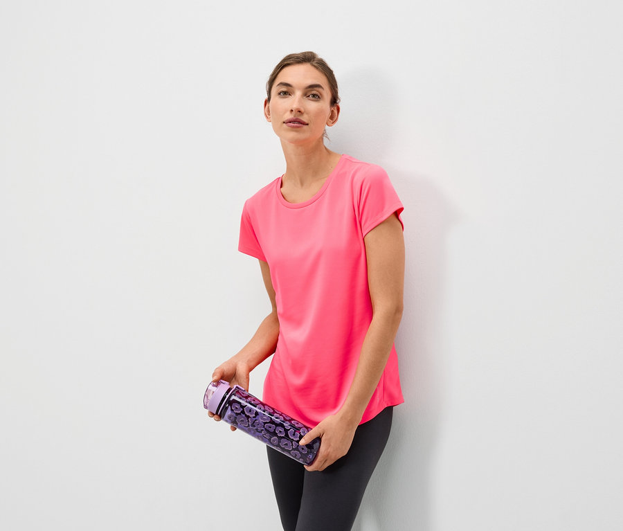 Une femme tenant une bouteille d'eau violette à motifs floraux, portant un t-shirt rose et un legging gris.