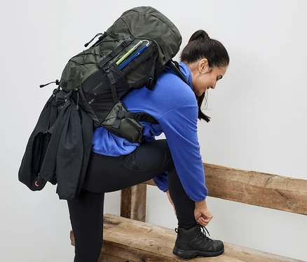 Une femme assise sur un banc noue ses lacets. Elle porte un sac à dos de randonnée de 40
mètres.