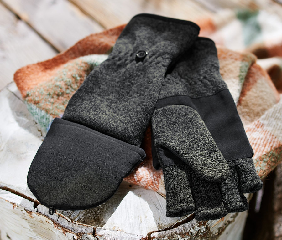 Une paire de mitaines avec moufles amovibles en maille polaire posée sur une bûche à côté d'un tas de bois.