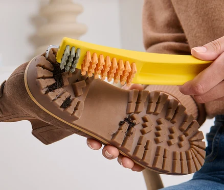 Femme nettoyant la semelle d'une chaussure marron avec une brosse à chaussures 3 en 1.