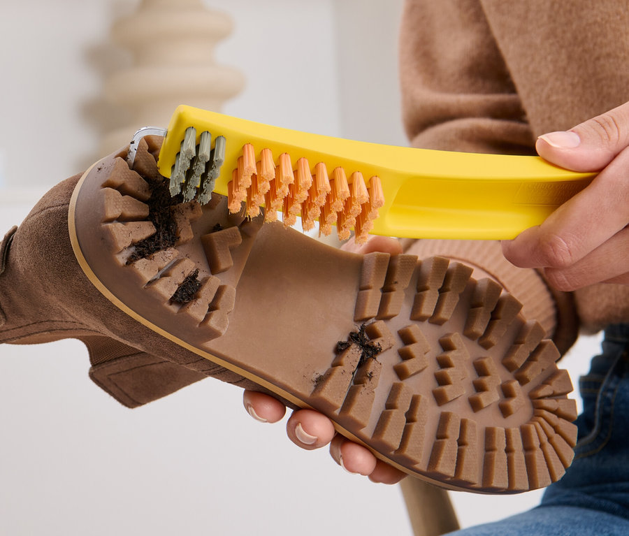 Femme nettoyant la semelle d'une chaussure marron avec une brosse à chaussures 3 en 1.