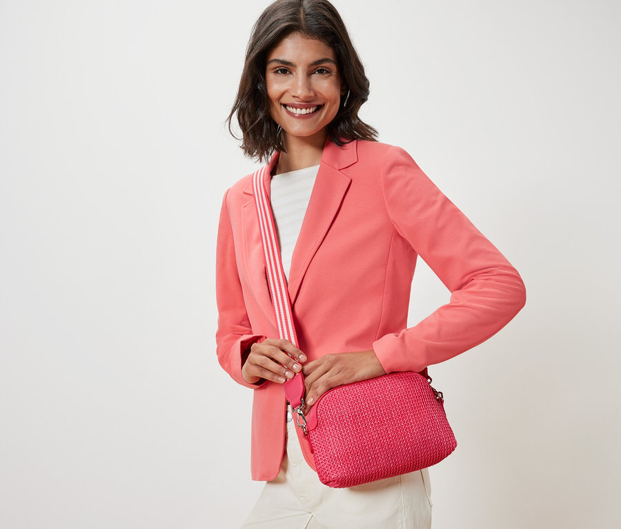 Femme avec une veste rose tenant un sac bandoulière rose.