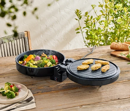 Des légumes dans une poêle noire et de la viande sur un gril sur une table en bois. Assiette de légumes, pain et beurre aux herbes en arrière-plan.