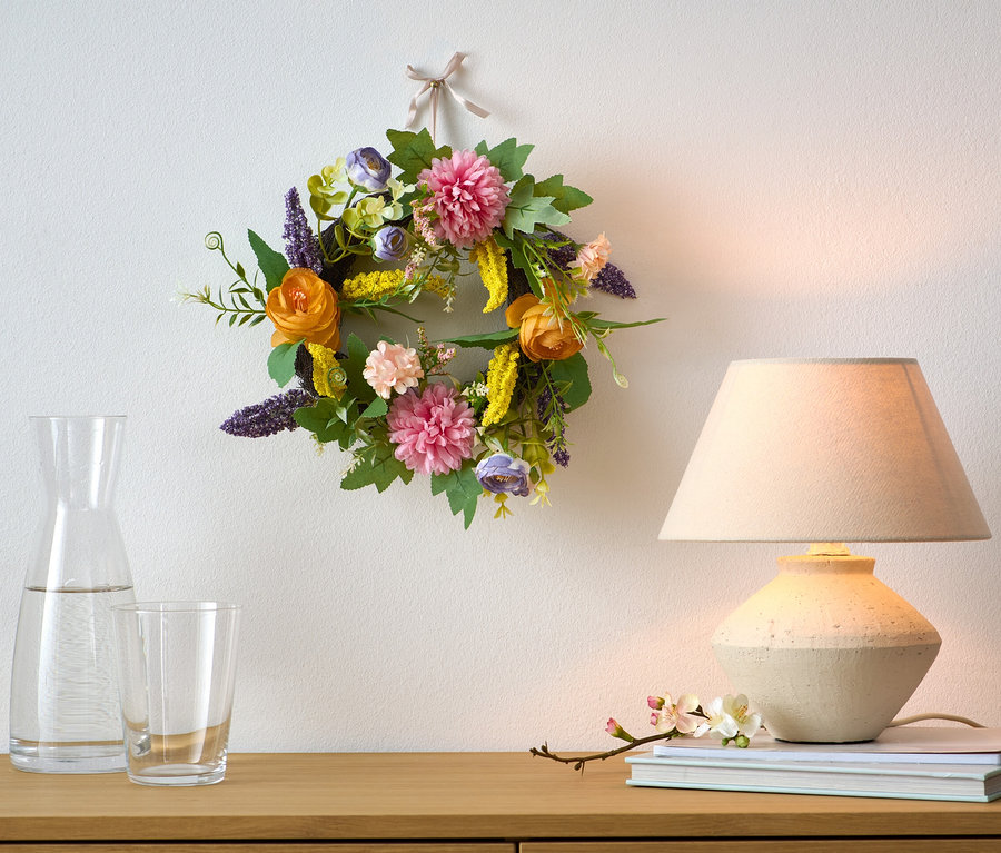 Une couronne décorative est accrochée au mur au-dessus d'une commode en bois.