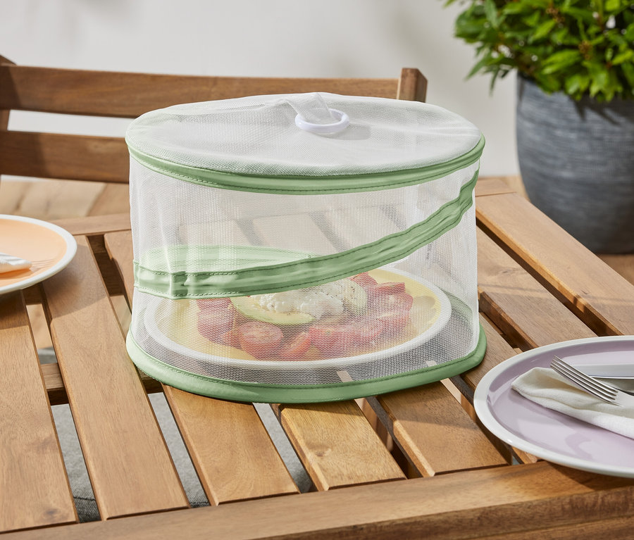 Une mini-cloche de protection pliable est posée sur une table en bois et protège une assiette de nourriture.