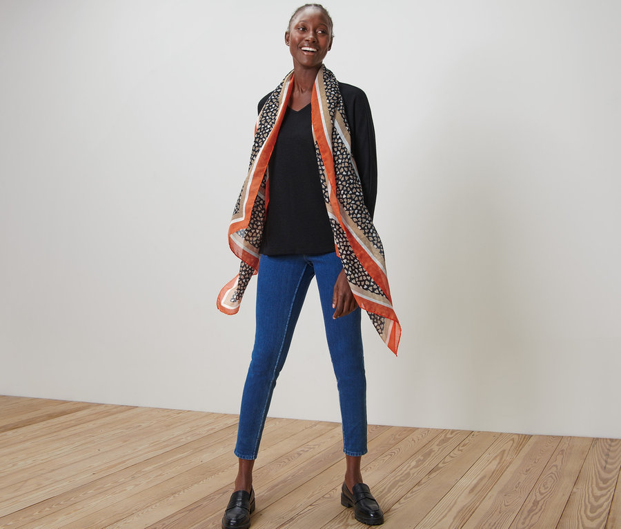 Une femme pose avec une écharpe tissée imprimée, un jean et des mocassins.