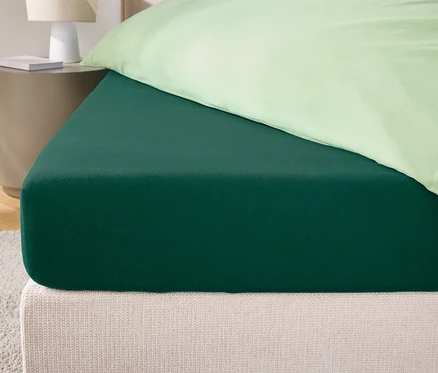 Gros plan d'un drap-housse vert sur un lit avec une tête de lit crème et une taie d'oreiller vert clair.