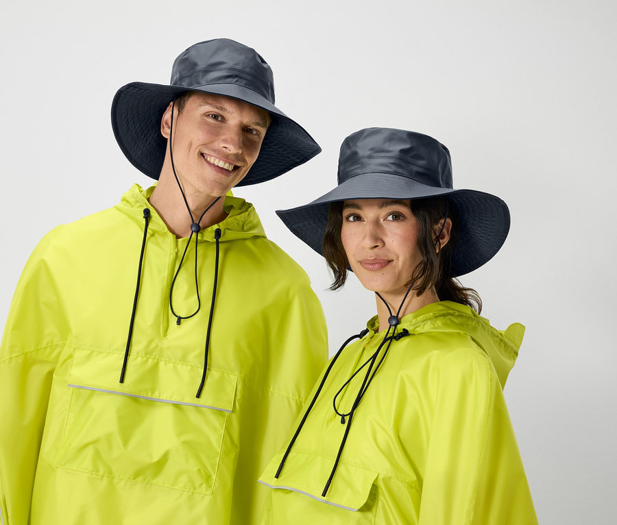 Un homme et une femme posent en imperméables jaunes assortis et chapeaux gris.