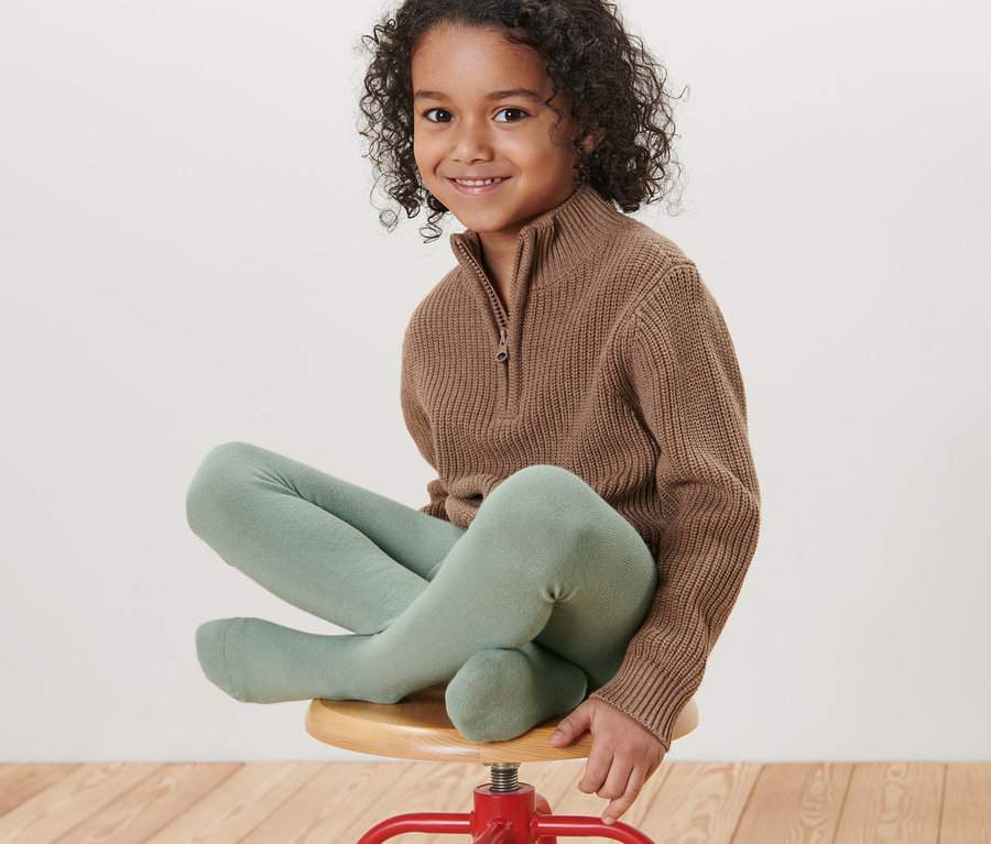 Une fille est assise sur un tabouret rouge et porte des collants pour enfant vert clair.