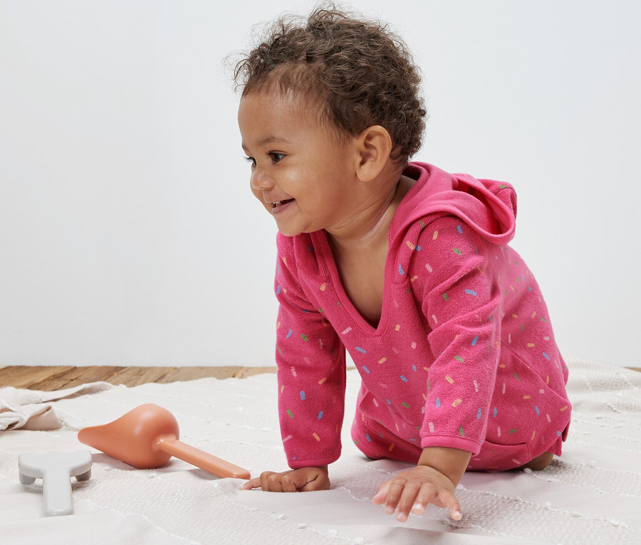 Un bébé rampe sur une couverture et porte un poncho rose en tissu éponge.
