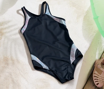 Maillot de bain pour enfant posé sur le sable à côté de sandales et d'une bouée verte.
