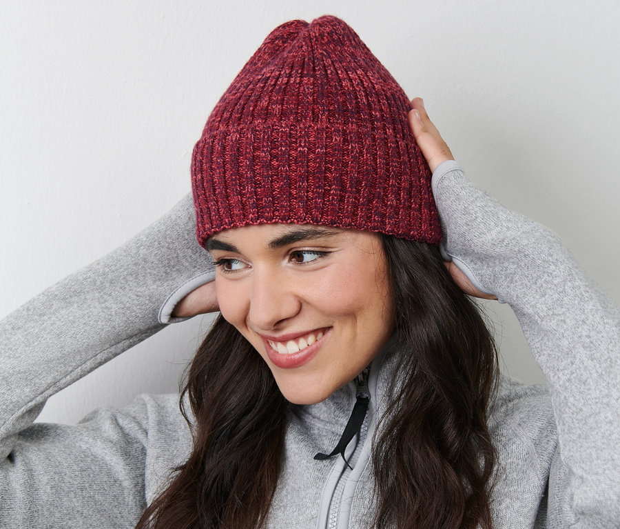 Une femme souriante ajuste son bonnet en maille sur sa tête.