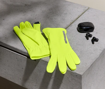 Deux gants jaune néon et des écouteurs noirs avec un étui sur une surface en béton.