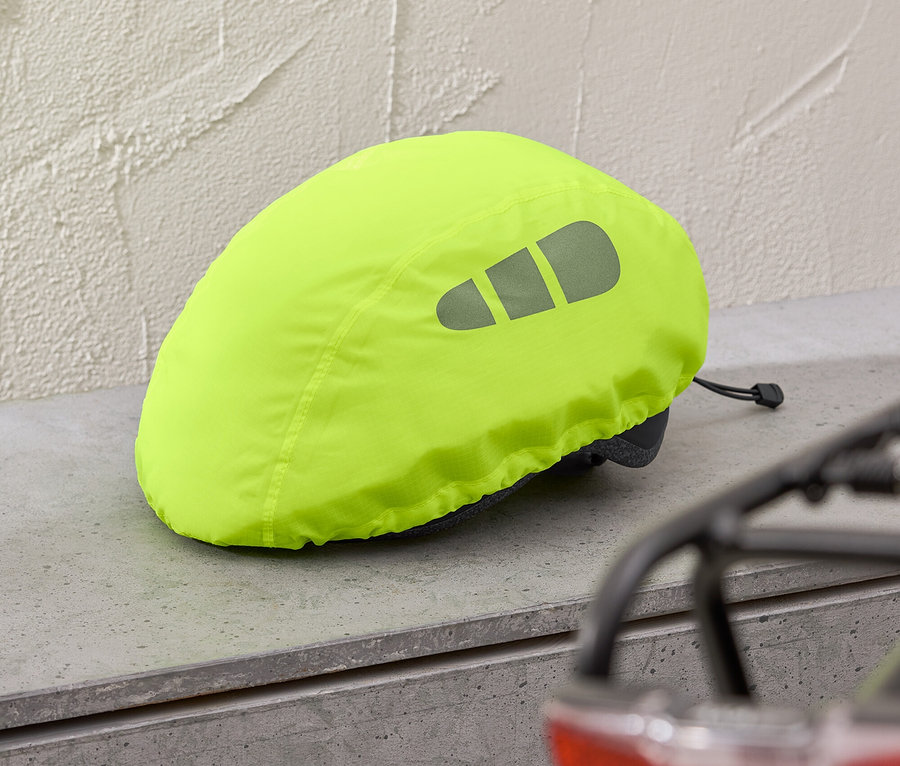 Une housse de casque jaune avec des réflecteurs repose sur une étagère grise, un feu de vélo rouge est visible en arrière-plan.