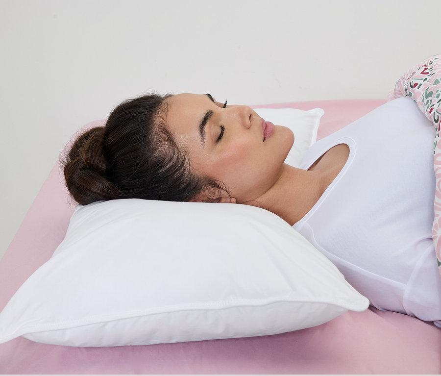 Femme dormant sur un oreiller à eau irisette® blanc sur un drap rose.