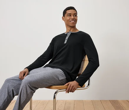 Un homme est assis sur une chaise, portant un t-shirt noir à manches longues et un pantalon de survêtement gris.