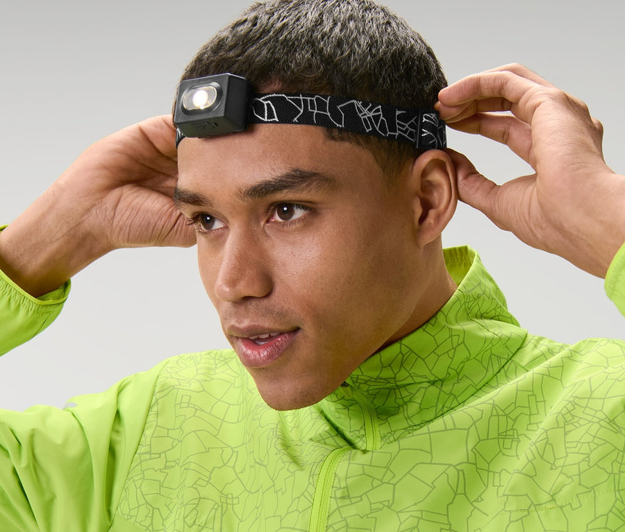 Un homme ajuste une lampe frontale sur son front et porte une veste verte.