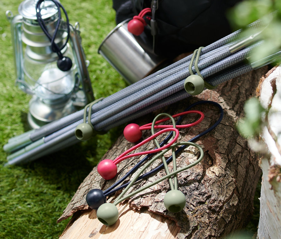 Sur une bûche en bois sont posés 12 tendeurs en caoutchouc avec boule, à côté d'eux une lanterne, un gobelet en métal, des barres et un sac à dos.