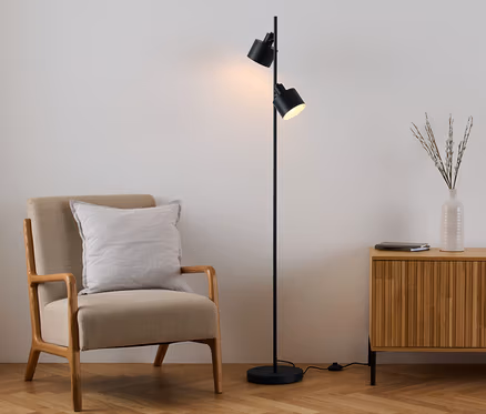 Un fauteuil avec un coussin est placé à côté d'un lampadaire noir et d'une commode en bois.