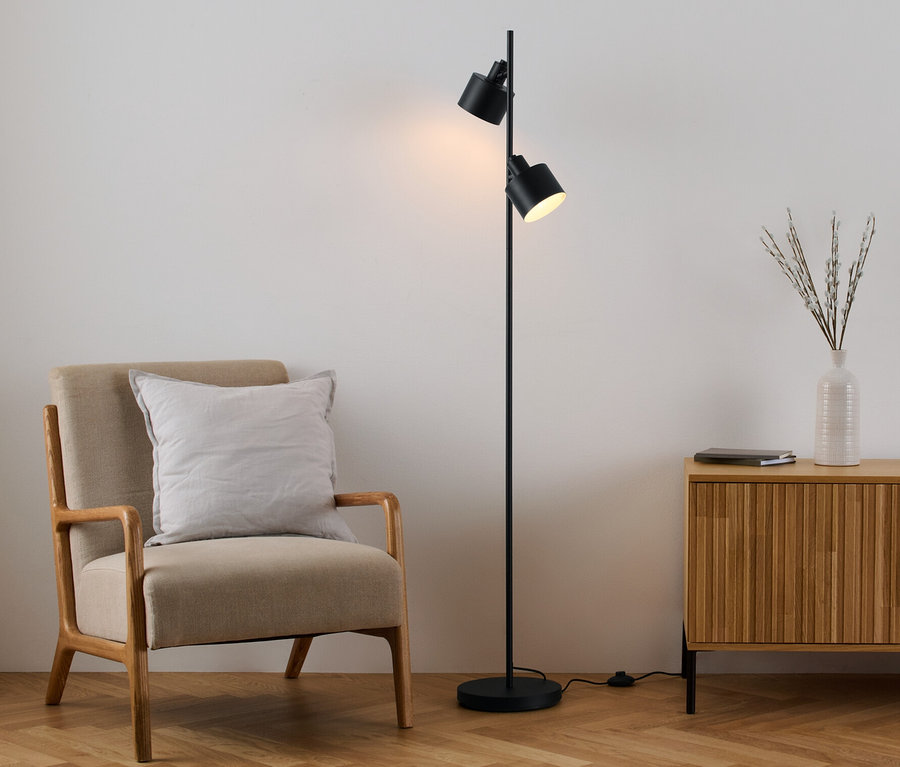 Un fauteuil avec un coussin est placé à côté d'un lampadaire noir et d'une commode en bois.