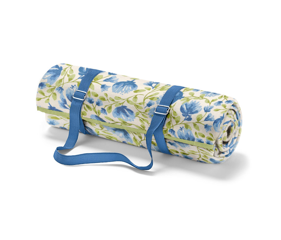 Une petite nappe de pique-nique enroulée avec des fleurs bleues et des tiges vertes, fixée par des sangles bleues.