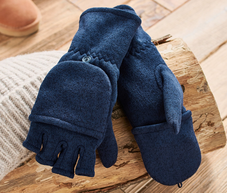 Des moufles convertibles en polaire tricotée bleu foncé sont posées sur une bûche à côté d'un bonnet et de bottes marron.