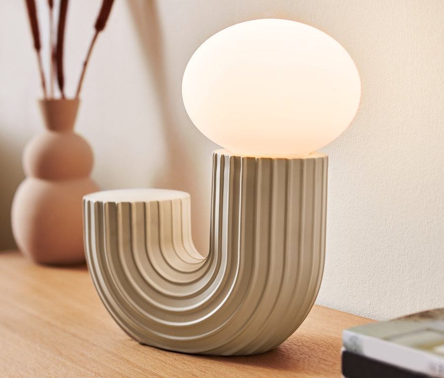 Une lampe de bureau design à LED est posée sur une table en bois à côté d'un vase et de livres.
