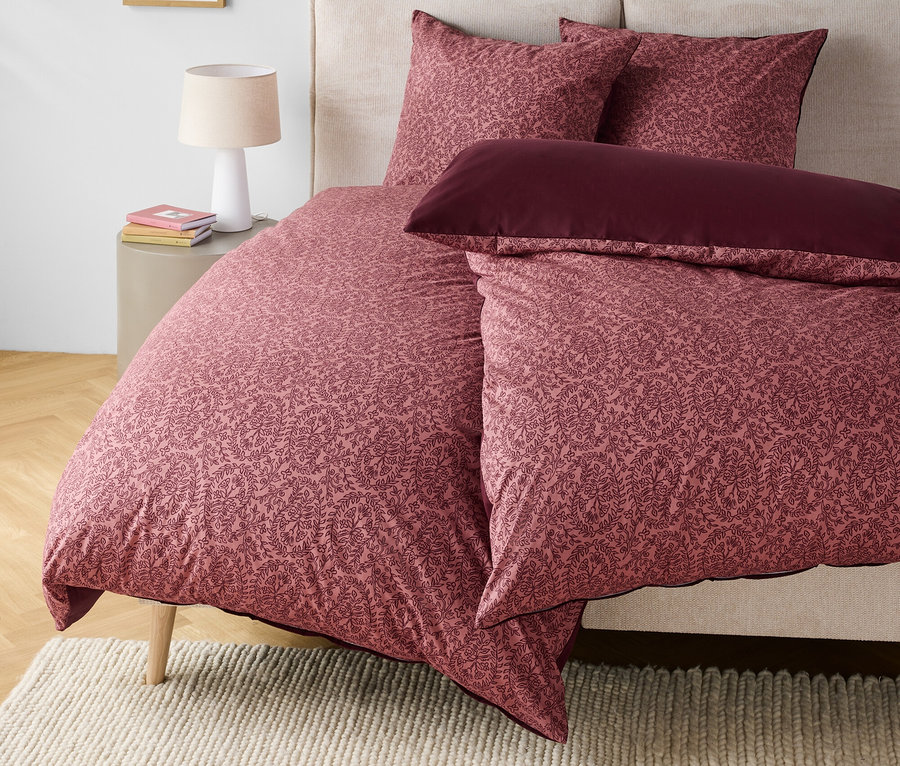 Linge de lit à motif floral dans les tons rose et bordeaux sur un lit avec une tête de lit beige.