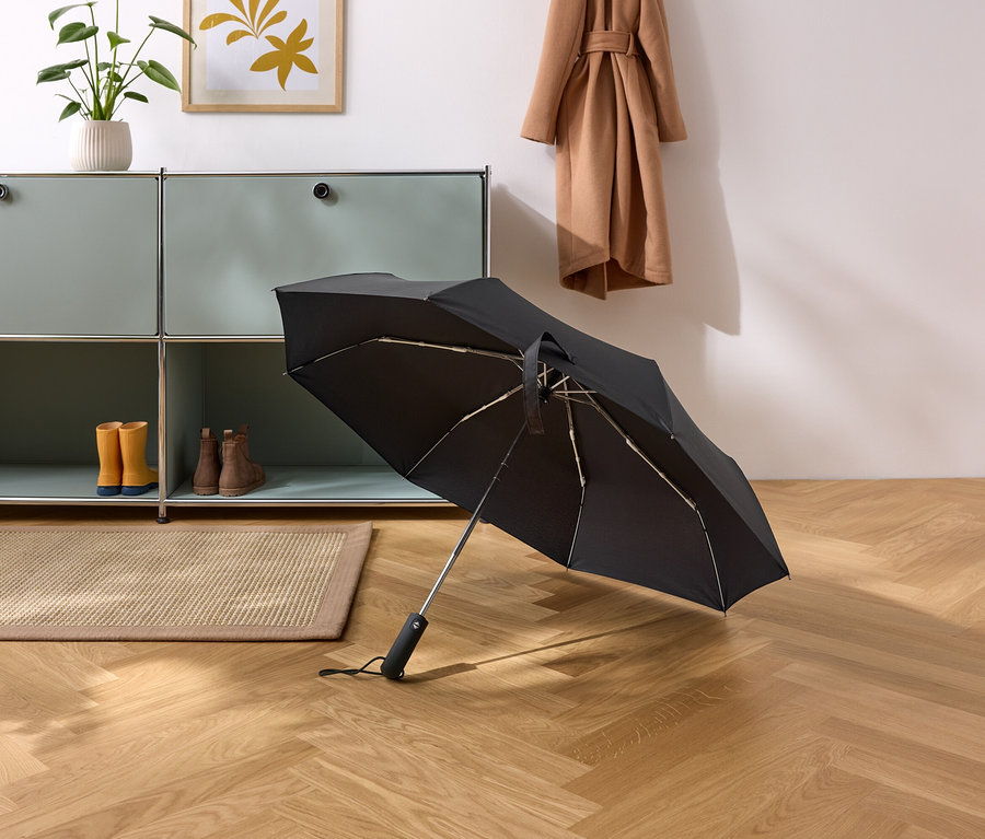 Un parapluie noir repose sur un parquet dans un couloir.