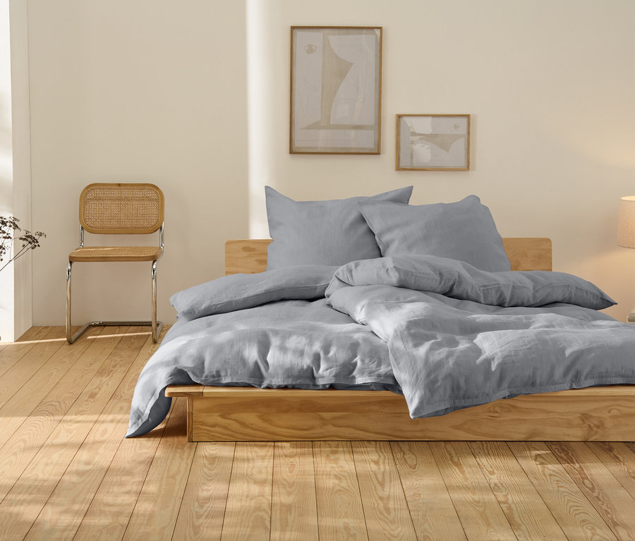 Linge de lit en lin gris, très grand, sur un lit en bois.