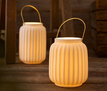 Deux lanternes blanches avec des poignées dorées posées sur une table en bois.