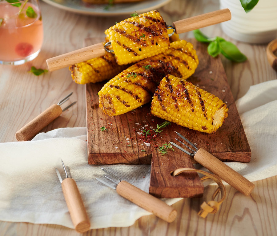 Maïs grillé sur une planche à découper en bois avec 8 piques à maïs.
