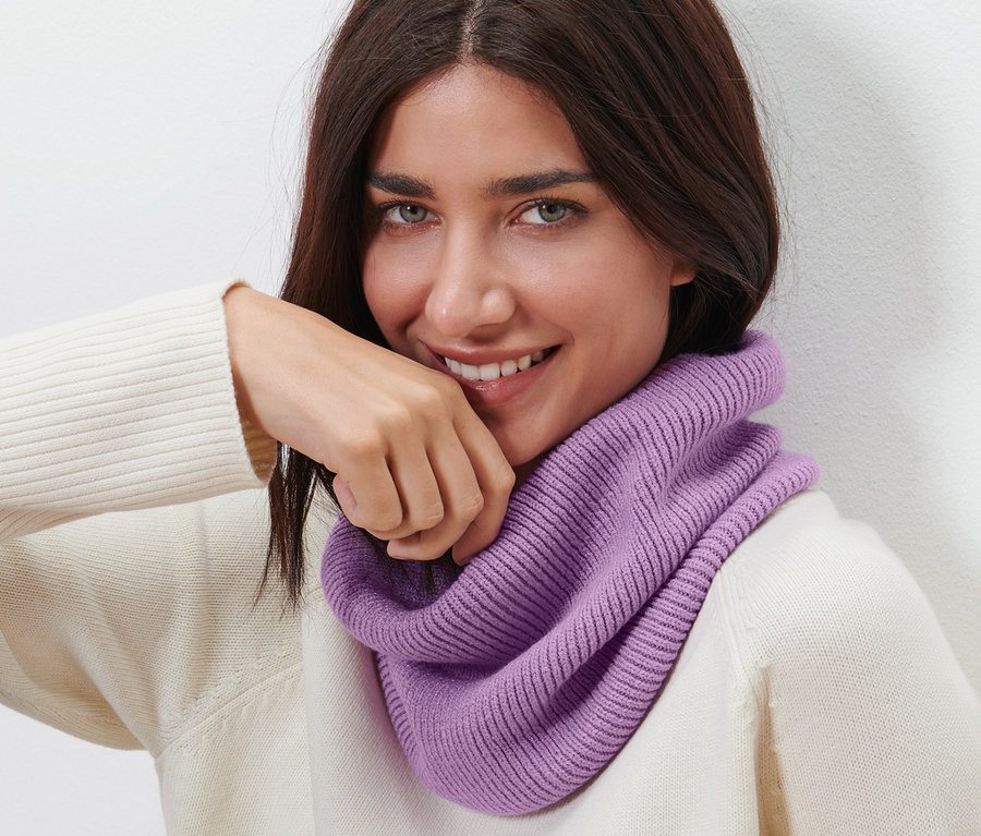 Une femme brune souriante porte une écharpe tube en maille.