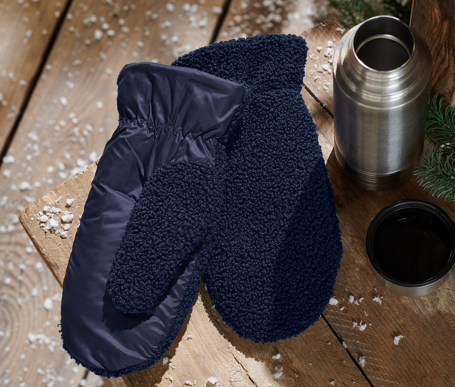 Sur une table en bois se trouvent des moufles bleues, une thermos et une tasse.