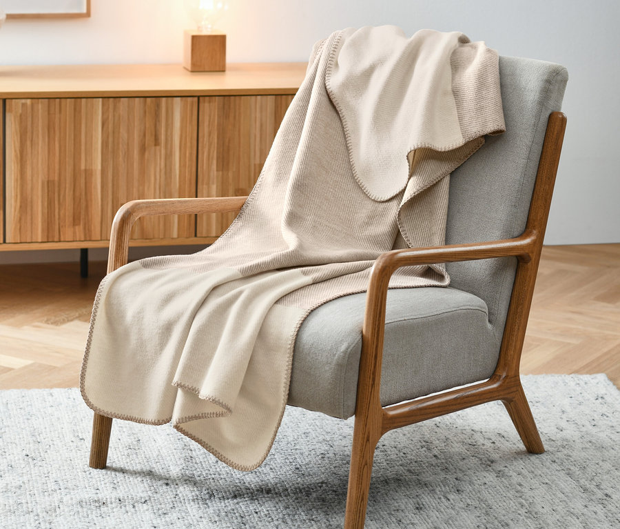 Couverture beige drapée sur un fauteuil gris.