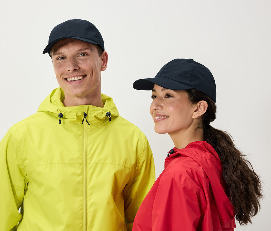 Un homme et une femme souriants portent des casquettes de baseball bleu marine et des imperméables vert citron et rouge.