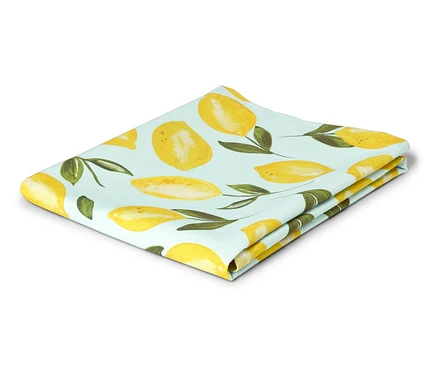Un torchon plié bleu clair avec un motif de citrons jaunes et de feuilles vertes est posé sur un fond blanc.