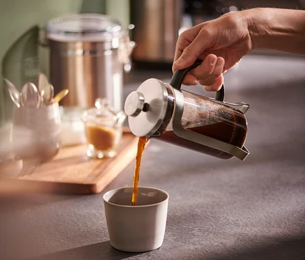 Une main verse du café d'une cafetière à piston argentée de 300 ml dans une tasse.