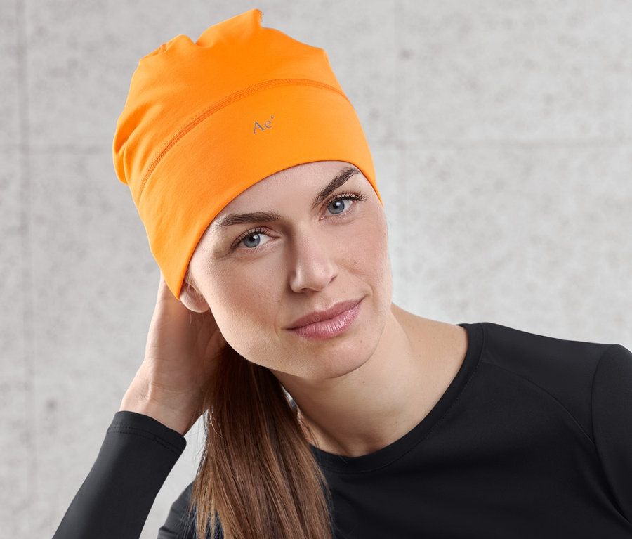 Femme assise portant un bonnet thermique orange fluo.