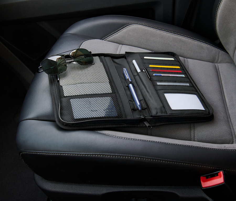 Un range-boîte à gants noir est posé ouvert sur un siège auto à côté de lunettes de soleil.