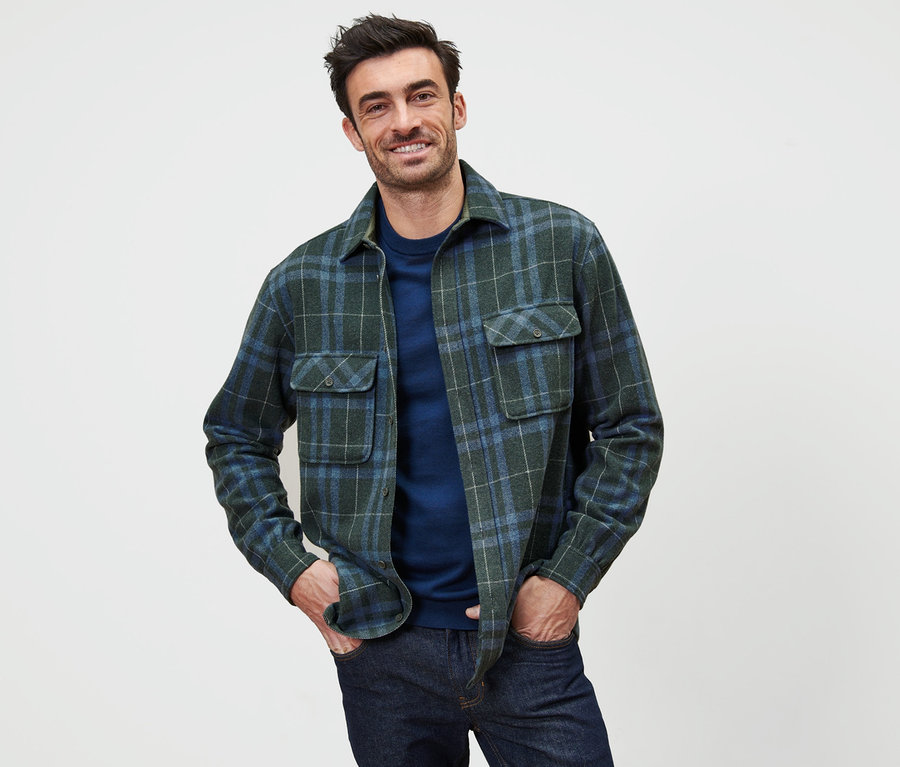 Un homme pose avec une veste-chemise en flanelle à carreaux verts et bleus.