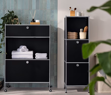 Une commode étroite en métal « CN3 » avec 2 compartiments à abattants et une commode métallique « CN3 » avec 1 tiroir et 1 compartiment à abattant sont dans la salle de bain. Des serviettes et des accessoires sont posés sur les commodes.