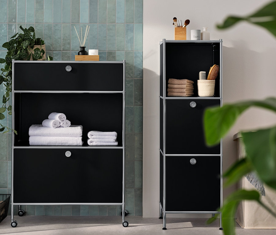 Une commode étroite en métal « CN3 » avec 2 compartiments à abattants et une commode métallique « CN3 » avec 1 tiroir et 1 compartiment à abattant sont dans la salle de bain. Des serviettes et des accessoires sont posés sur les commodes.