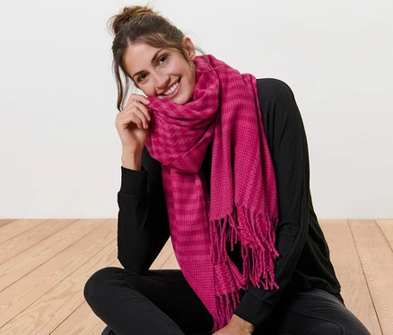 Une femme est assise par terre, les jambes croisées, et porte une écharpe tissée à franges.
