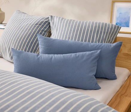 Sur un lit, il y a deux oreillers rectangulaires bleus et deux oreillers à rayures bleues et blanches.