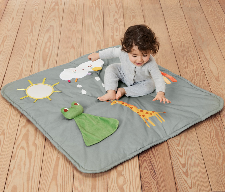 Bébé assis sur une couverture d’activités pour bébé avec des motifs de soleil, de nuages, de girafe et de grenouille.
