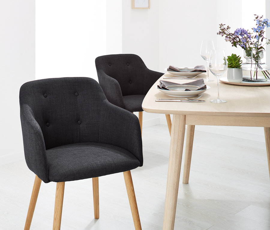 Deux chaises rembourrées anthracite avec accoudoirs et une table en bois avec des fleurs et des assiettes dans une salle à manger.