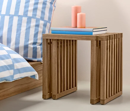 Tabouret extensible avec des livres et des bougies à côté du lit et d'un vase orange.